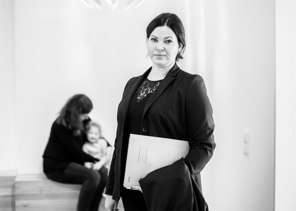SW Portrait Rechtsanwältin Kristina Grün. Im Hintergrund Mutter mit Kind