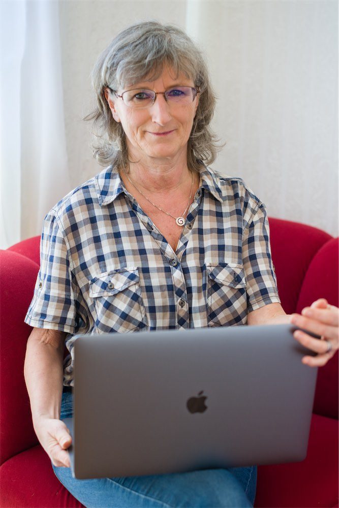 Portrait der Autorin Dagmar Hansen in einem roten Sessel mit Apple Macbook