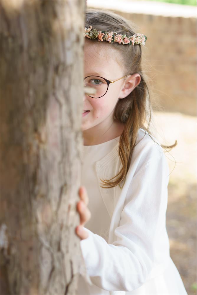 Kommunionskind Marla versteckt sich hinter einem Baumstamm